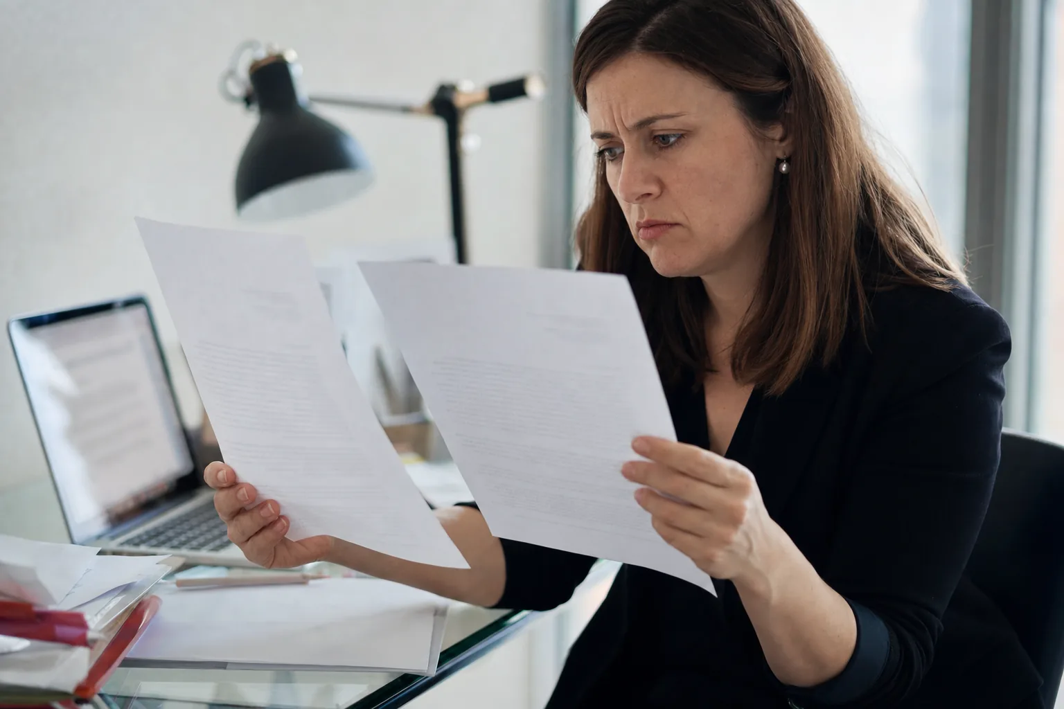 Una mujer compara con desconfianza dos cartas casi idénticas en su mesa de trabajo