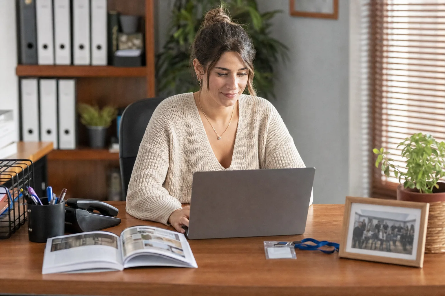 Una administrativa lee sonriente un correo muy personal en su portátil, con un folleto de la empresa y una foto del equipo sobre la mesa